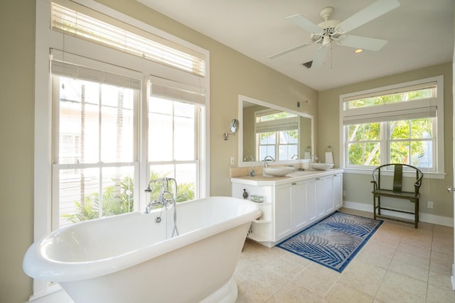 bathroom featuring double vanity, a ceiling fan, a sink, a freestanding tub, and baseboards