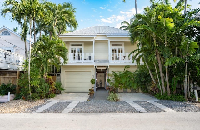 coastal home with an attached garage, a balcony, metal roof, and concrete driveway