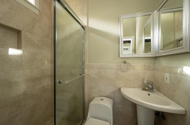 bathroom featuring a wainscoted wall, tile walls, toilet, a sink, and a shower stall