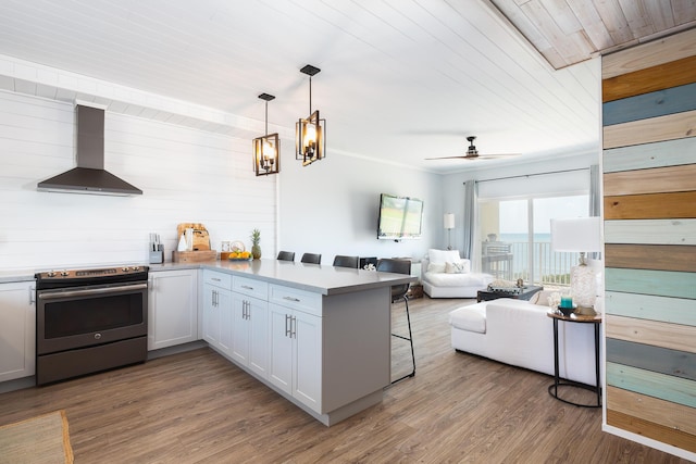 kitchen with white cabinetry, stainless steel electric range oven, kitchen peninsula, and wall chimney range hood