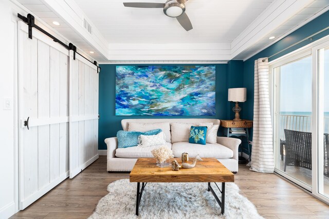 living room featuring wood-type flooring, a barn door, and ceiling fan