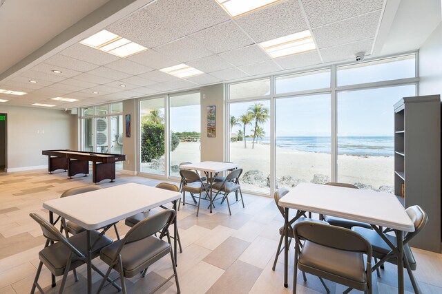 dining space featuring a water view, floor to ceiling windows, a drop ceiling, and a beach view