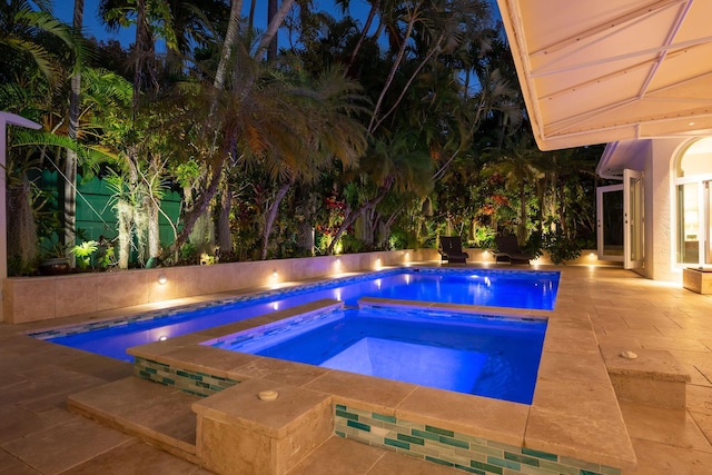 pool at night with an in ground hot tub, a patio, and a fenced in pool