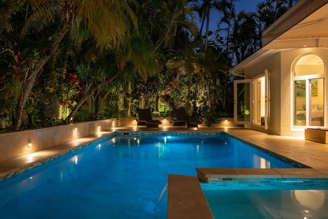 pool at night featuring an outdoor pool and a patio