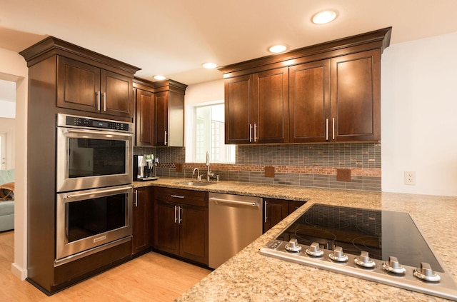 kitchen with appliances with stainless steel finishes, a sink, backsplash, and dark brown cabinetry