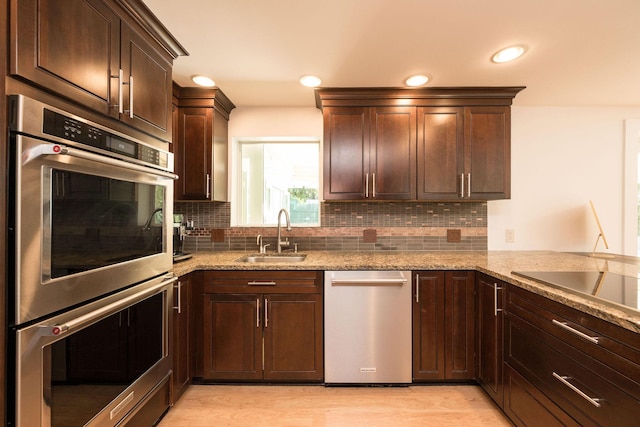 kitchen featuring decorative backsplash, appliances with stainless steel finishes, light stone counters, and a sink