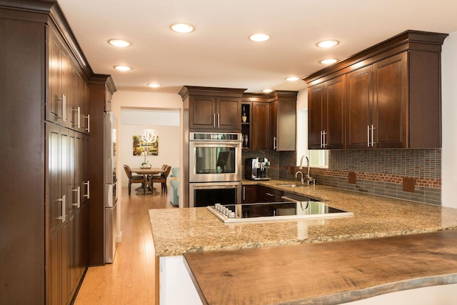 kitchen featuring appliances with stainless steel finishes, a peninsula, dark brown cabinets, light wood-type flooring, and a sink