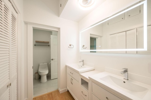 bathroom featuring double vanity, a closet, toilet, a sink, and wood finished floors