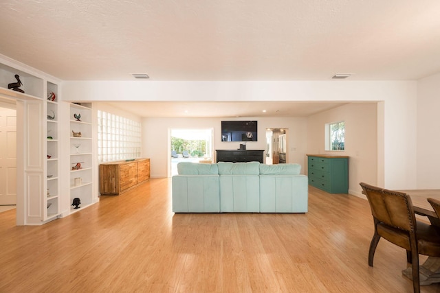 living room with light wood-type flooring, visible vents, and a wealth of natural light