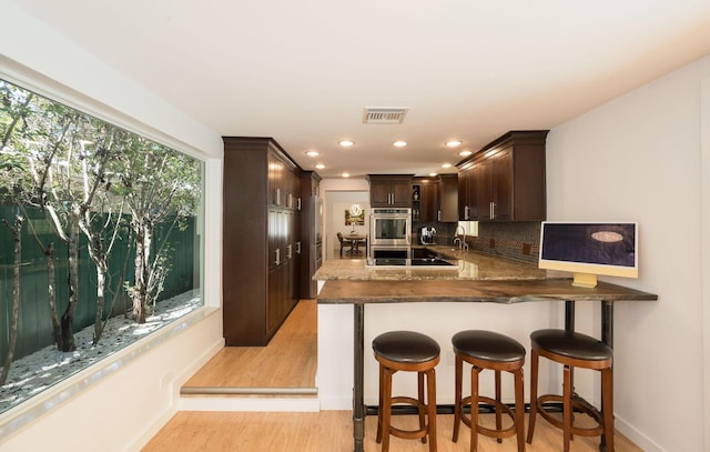 kitchen featuring double oven, light wood-style flooring, dark brown cabinetry, visible vents, and tasteful backsplash