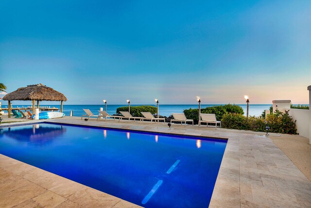 pool at dusk with a gazebo, a patio area, and a water view