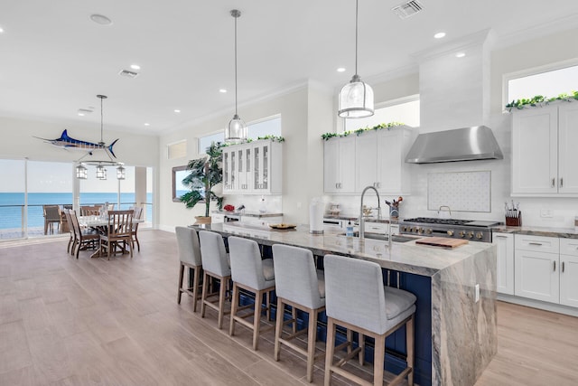 kitchen with sink, white cabinets, a water view, light stone countertops, and a center island with sink