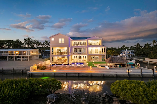 back house at dusk with a water view, a patio, and a balcony