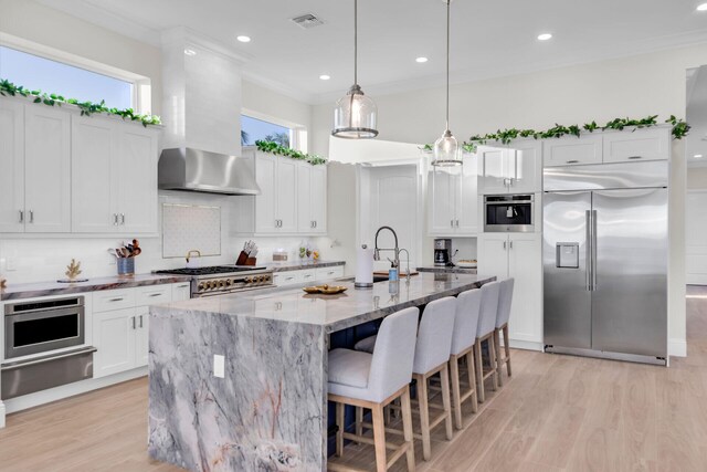 kitchen with built in appliances, light stone countertops, white cabinets, and a center island with sink