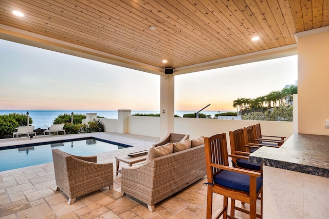 patio terrace at dusk featuring a bar, an outdoor living space, and a water view