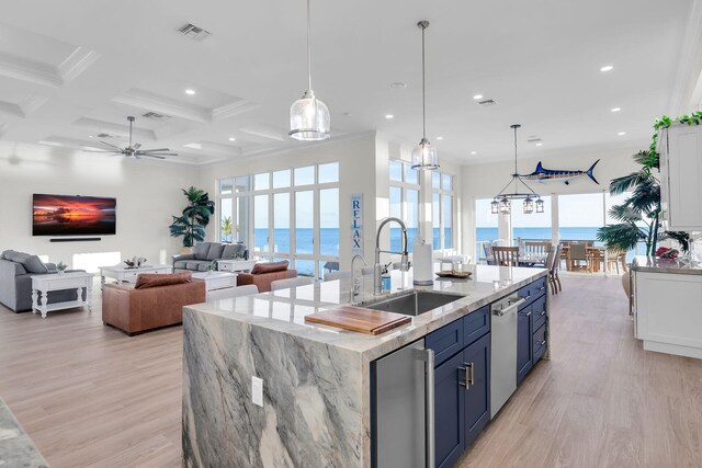 kitchen featuring blue cabinets, sink, a water view, decorative light fixtures, and a center island with sink