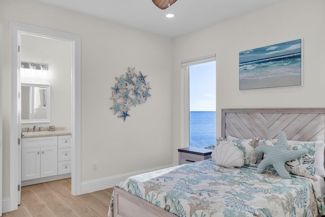 bedroom with ensuite bathroom, a water view, sink, and light wood-type flooring