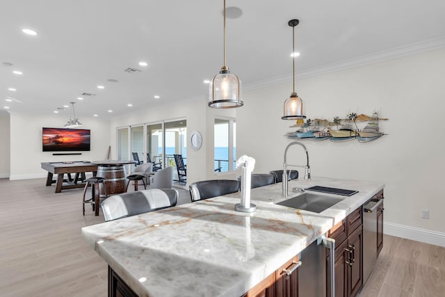 kitchen featuring an island with sink, light stone countertops, sink, and ornamental molding