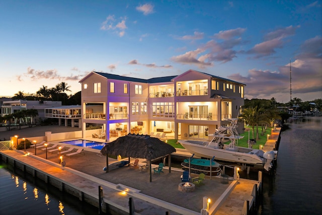 back house at dusk featuring a water view, a balcony, and a patio area