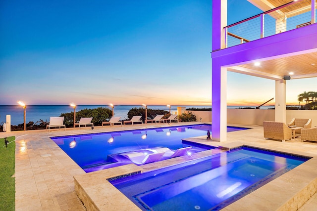 pool at dusk featuring an in ground hot tub, a water view, and a patio area