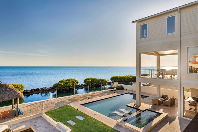 pool at dusk with a hot tub, a water view, an outdoor hangout area, and a patio area