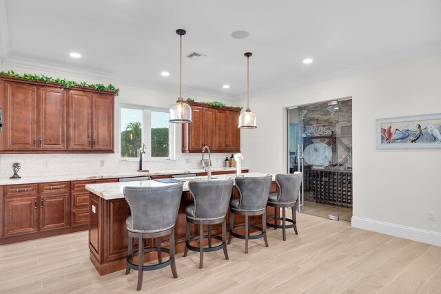 kitchen featuring pendant lighting, light stone counters, light hardwood / wood-style floors, a center island with sink, and decorative backsplash