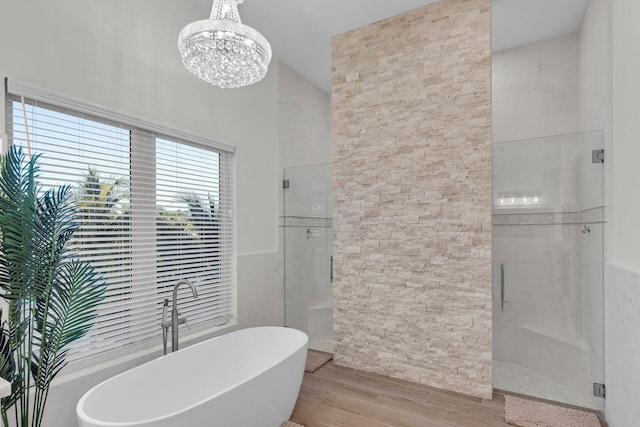 bathroom with independent shower and bath, wood-type flooring, and an inviting chandelier