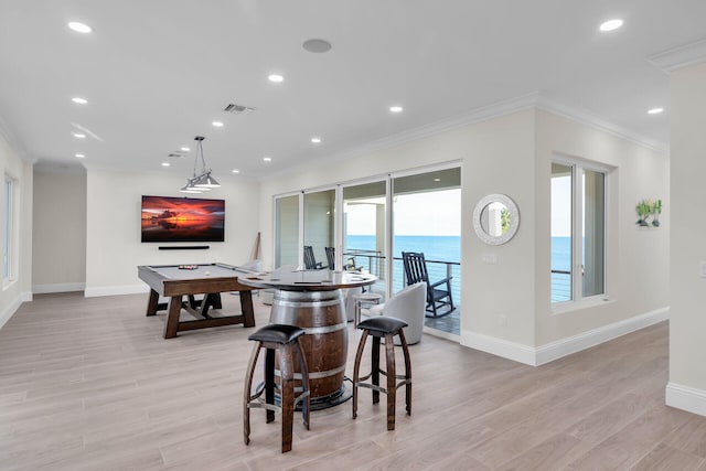 interior space featuring crown molding, a kitchen bar, pendant lighting, and light wood-type flooring