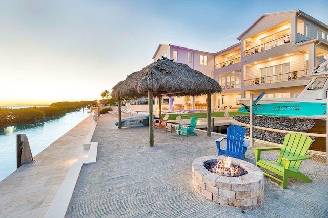 patio terrace at dusk featuring a gazebo, a water view, and a fire pit