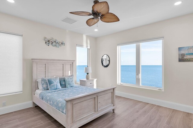 bedroom with ceiling fan, a water view, and light hardwood / wood-style floors