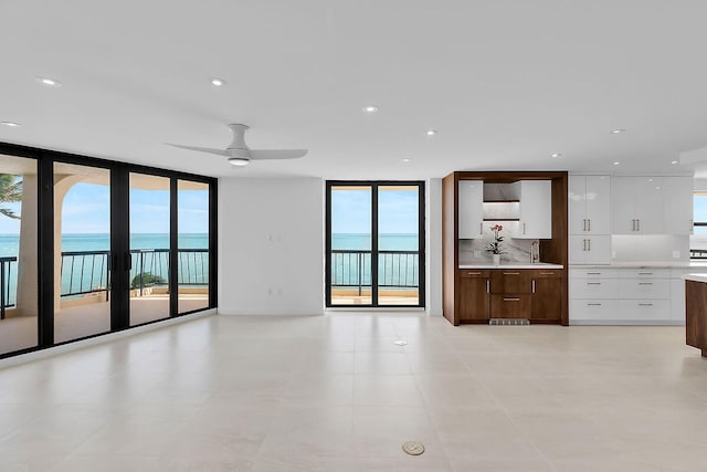 unfurnished living room featuring a water view, recessed lighting, a sink, and expansive windows