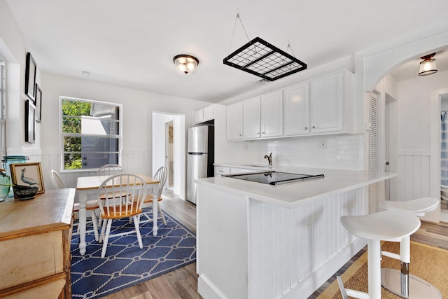 kitchen featuring sink, white cabinetry, stainless steel fridge, kitchen peninsula, and hardwood / wood-style flooring