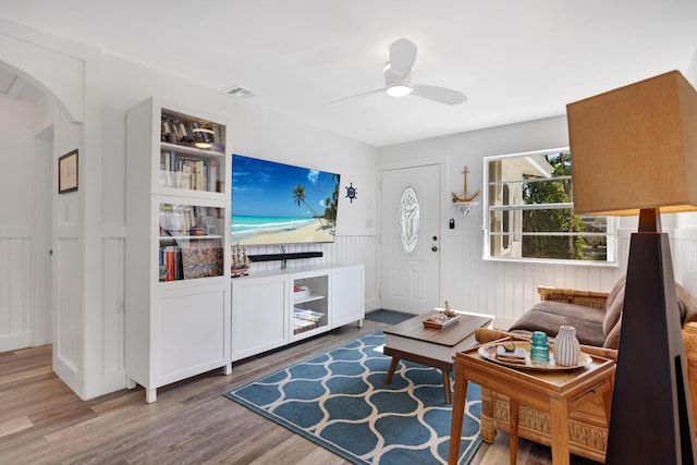 living area featuring a ceiling fan, visible vents, wood finished floors, and arched walkways