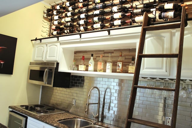 interior space featuring stovetop, sink, white cabinets, and decorative backsplash
