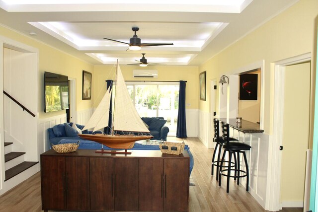 living room featuring an AC wall unit, light hardwood / wood-style floors, and a raised ceiling