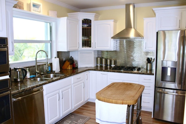 kitchen featuring sink, crown molding, appliances with stainless steel finishes, white cabinets, and wall chimney exhaust hood