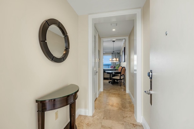 corridor featuring baseboards and a notable chandelier