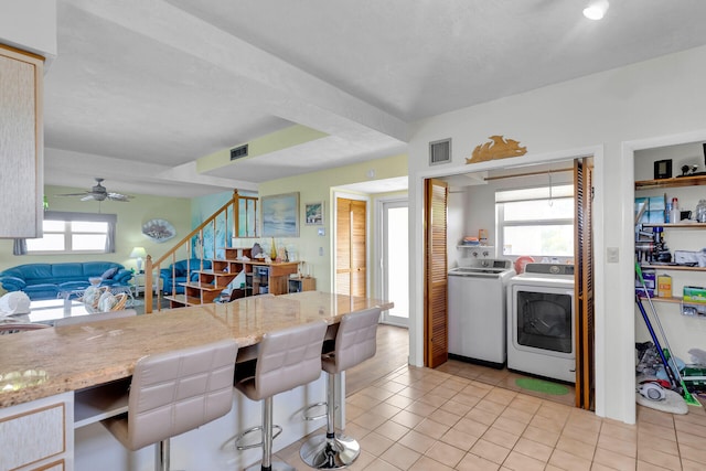 kitchen featuring light tile patterned flooring, a kitchen breakfast bar, ceiling fan, light stone counters, and washing machine and dryer