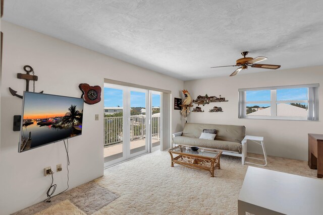 living room featuring ceiling fan, light carpet, and a textured ceiling