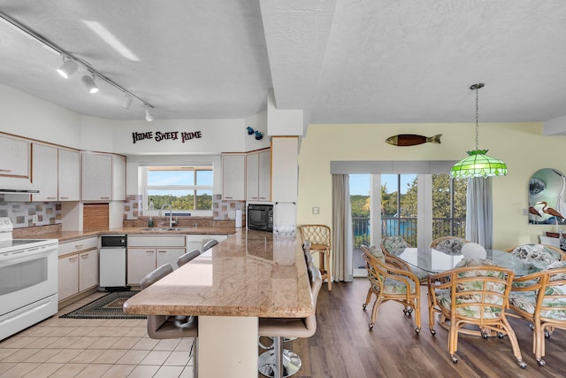 kitchen with pendant lighting, sink, a kitchen breakfast bar, decorative backsplash, and white appliances