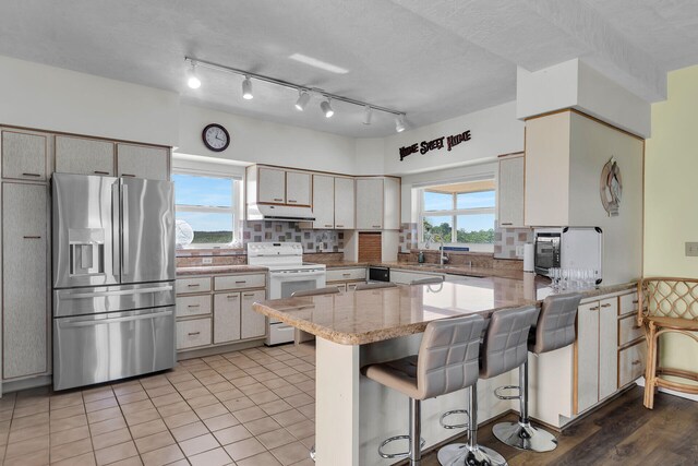 kitchen with a breakfast bar area, white range with electric stovetop, stainless steel refrigerator with ice dispenser, decorative backsplash, and kitchen peninsula