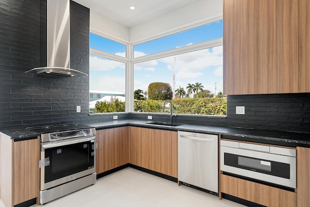 kitchen featuring wall chimney exhaust hood, sink, tasteful backsplash, appliances with stainless steel finishes, and dark stone counters