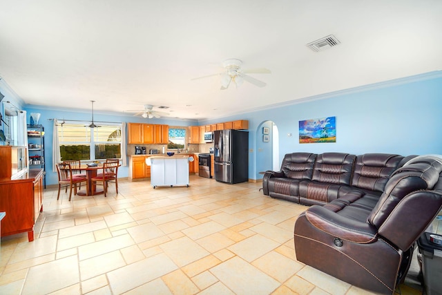 living room with stone finish flooring, visible vents, a ceiling fan, and ornamental molding