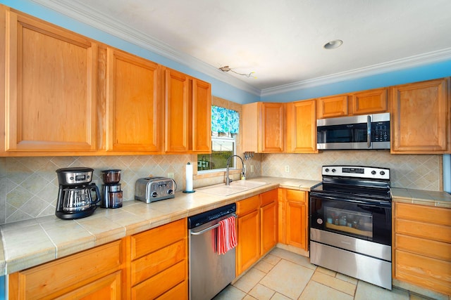 kitchen featuring tile countertops, ornamental molding, stainless steel appliances, and a sink