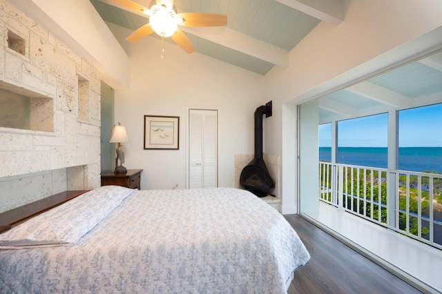 bedroom featuring ceiling fan, a water view, lofted ceiling with beams, dark hardwood / wood-style flooring, and a wood stove