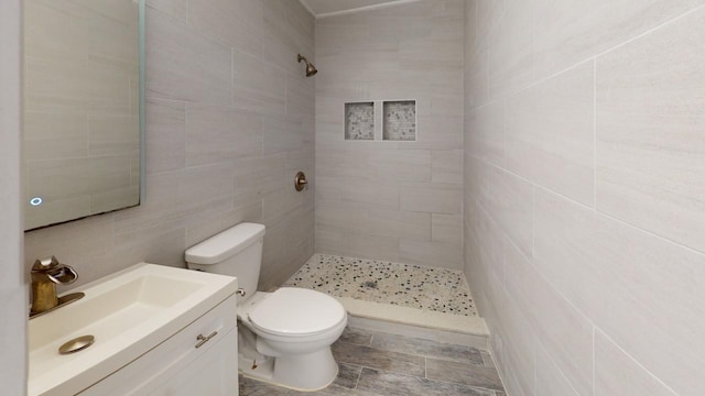 bathroom featuring vanity, a tile shower, tile walls, and toilet