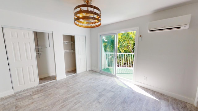 unfurnished bedroom featuring two closets, a wall mounted AC, access to outside, a notable chandelier, and light hardwood / wood-style floors