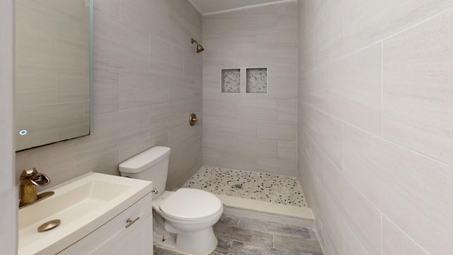 bathroom featuring a tile shower, vanity, tile walls, and toilet