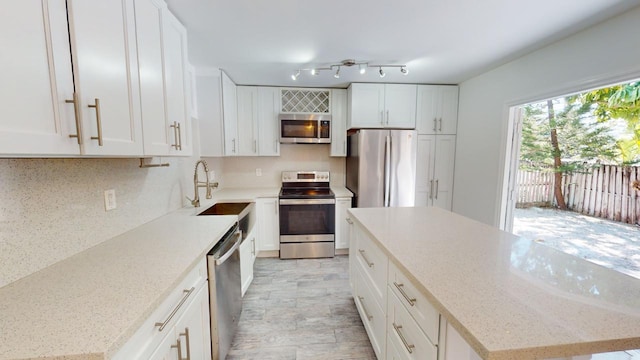 kitchen with sink, light stone counters, appliances with stainless steel finishes, a kitchen island, and white cabinets