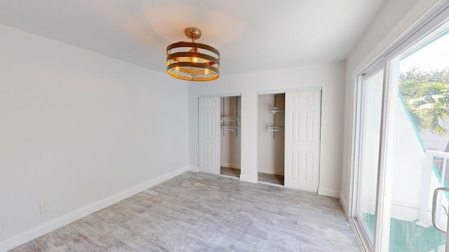 unfurnished bedroom featuring a notable chandelier, light hardwood / wood-style flooring, and two closets